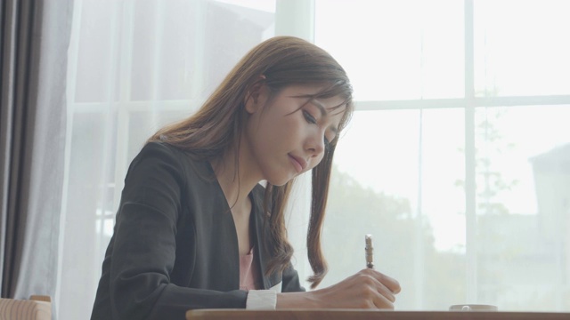 幸福亚洲商业女性正在做笔记，写和交谈的智能手机，放松和愉快的工作在办公室视频素材