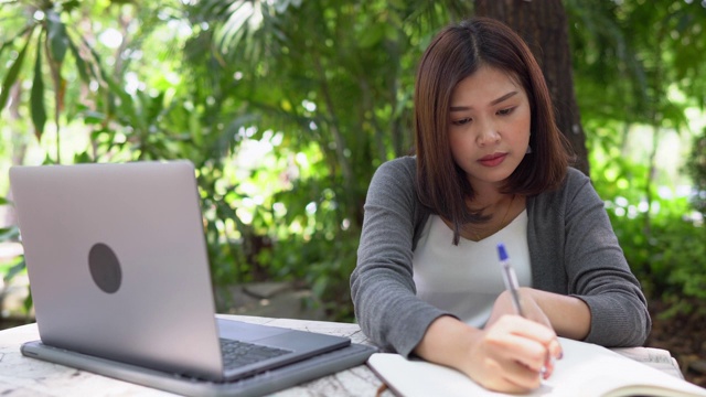 亚洲女学生在户外学习使用笔记本电脑和写笔记本在大学公园视频素材