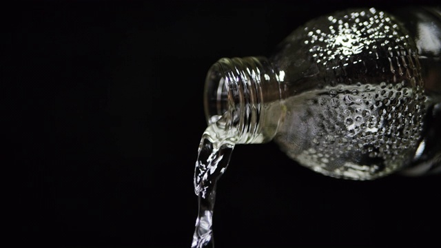 慢镜头近景拍摄干净的水从打开的玻璃瓶在黑色的背景侧视图视频素材