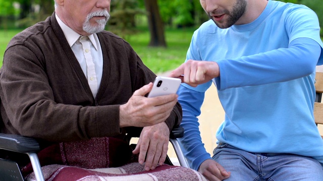 微笑的男性志愿者向残障老人讲解如何使用手机app，关爱老人视频素材