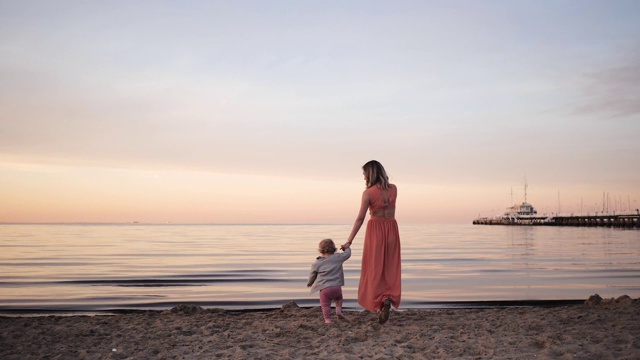 年轻的女人妈妈穿着衣服走在海边在夕阳下与一个小女儿视频素材