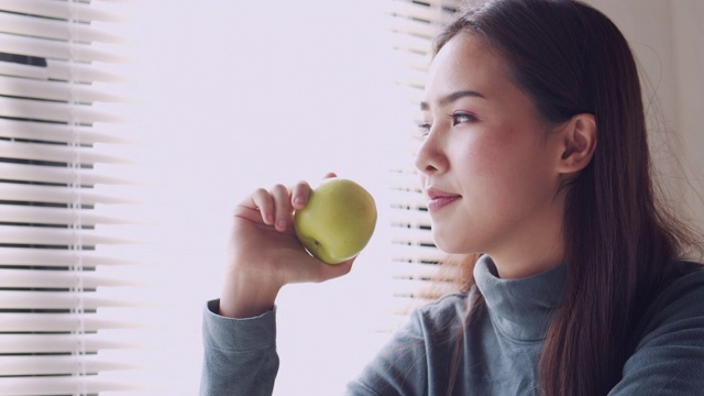 亚洲妇女微笑和吃苹果在家，健康和生活方式的概念视频素材