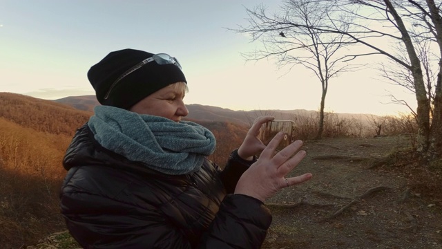 一个成熟的女人用智能手机在切罗哈拉公路上拍摄南塔哈拉国家森林。秋天寒冷的晚上。视频素材