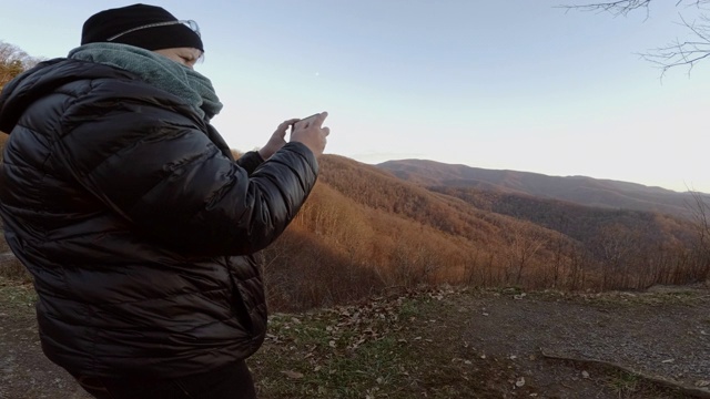 一个成熟的女人用智能手机在切罗哈拉公路上拍摄南塔哈拉国家森林。秋天寒冷的晚上。视频素材