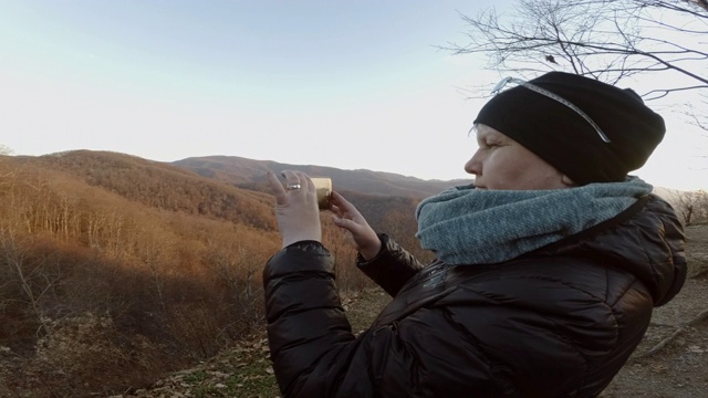 一个成熟的女人用智能手机在切罗哈拉公路上拍摄南塔哈拉国家森林。秋天寒冷的晚上。视频素材