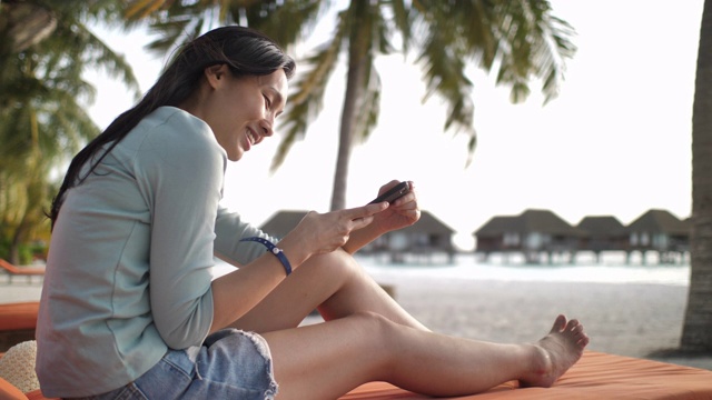 一个年轻女子在海滩用手机发短信视频素材