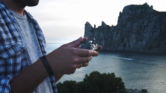 无人机遥控器，手和遥控视图的一个无人机飞行员操作员。在旅途中，这个年轻人在海滩附近操控无人机。欣赏美丽的海景和山景视频素材