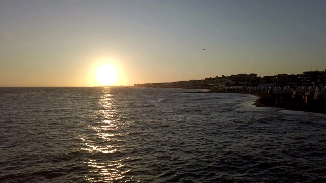 海面上的夕阳映在海面上，一架飞机飞过城市上空视频素材