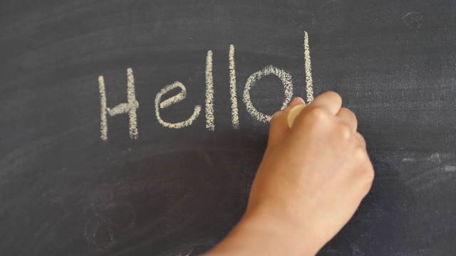 这是一个女人用一大块黄色粉笔在布满灰尘的旧黑板或黑板上写“hello”和“感叹号”的特写。视频素材