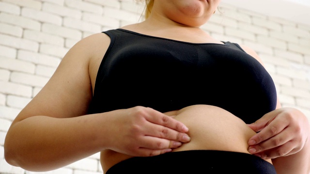超重的年轻女子在运动服装夹她的腹部脂肪视频素材