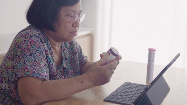 亚洲妇女拿着药瓶，在起居室里用药片说话。视频素材