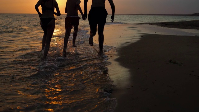 快乐的朋友们在希腊的夏日沙滩上跑步，在美丽的夕阳下游泳视频素材