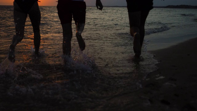 快乐的朋友们在希腊的夏日沙滩上跑步，在美丽的夕阳下游泳视频素材