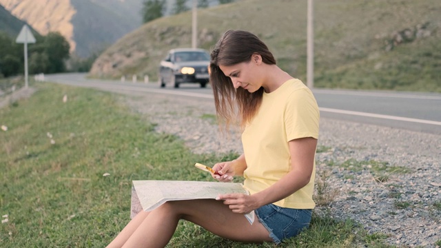 美丽的女孩游客看地图的道路，而坐在高速公路在夏天阳光明媚的天气。侧视图视频素材