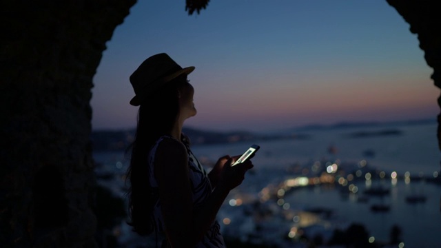 希腊米科诺斯，一位年轻女性在户外使用智能手机的侧面图视频素材