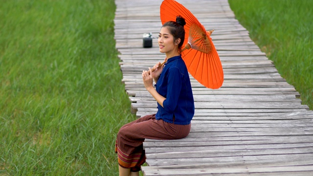 美丽的泰国女人穿着传统风格拿着红色伞在户外。视频素材