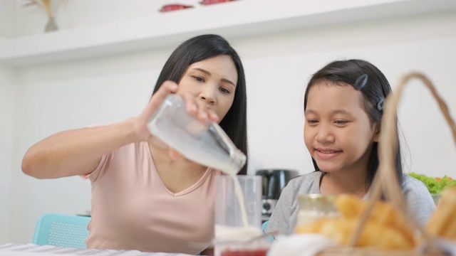 慢镜头亚洲母亲早上在厨房给女儿倒牛奶视频素材