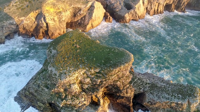 飞过葡萄牙阿尔加维海岸平坦的岩石。无数的海鸥在岩石周围飞来飞去。日落时，泛着泡沫的绿松石般的海洋闪耀着金色。空中,UHD视频素材