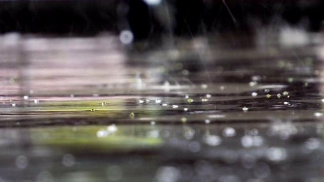 近距离的视频镜头雨点落下来的大理石表面的水面溅起波纹在大雨，潮湿的雨天天气自然背景，音频包括视频素材