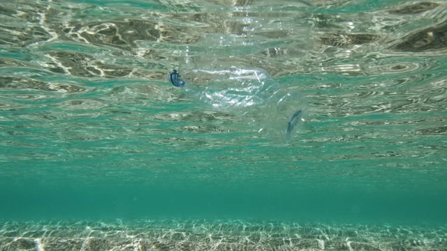 在浅海中废弃的塑料水瓶，5倍慢镜头拍摄。视频下载