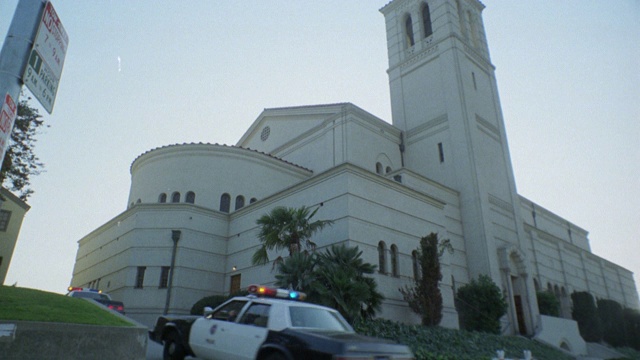 四辆警车开着警笛，闪烁着警灯在城市街道上超速行驶。警车右转进入多层建筑的车道，可能是政府大楼或教堂。视频素材