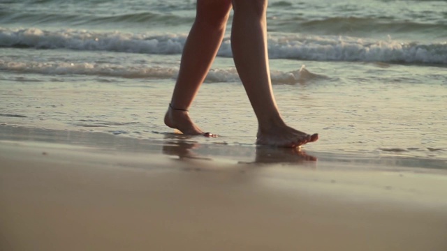 女人走在海滩上的日落腿特写视频素材