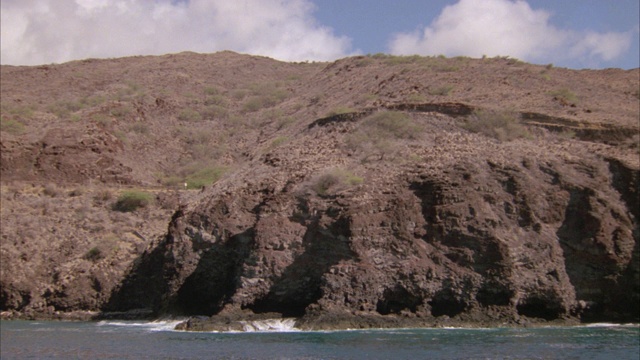 宽角度的海浪撞击岩石海岸与贫瘠的山或悬崖在bg。海洋。视频素材