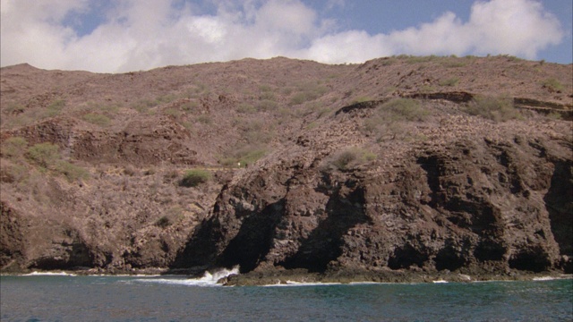 宽角度的海浪撞击岩石海岸与贫瘠的山或悬崖在bg。海洋。沿着海岸行驶的汽车。视频素材