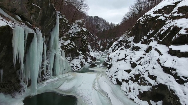 飞越峡谷底部的冬季河流。冰柱悬挂在峡谷的石墙上视频素材