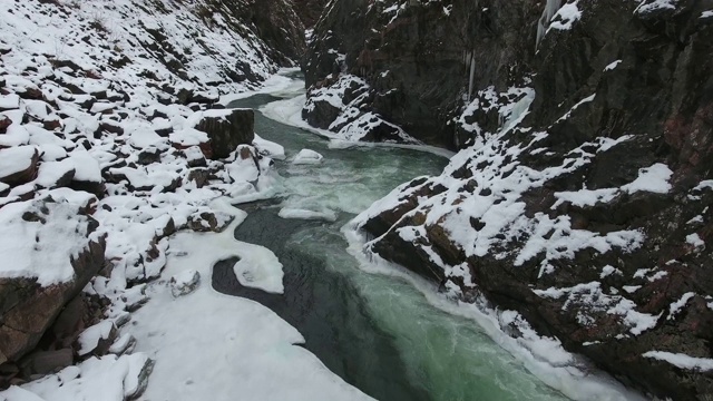 在俄罗斯高加索山脉的一个被白雪覆盖的峡谷底部，一条湍急的山间溪流的碧绿的水视频素材