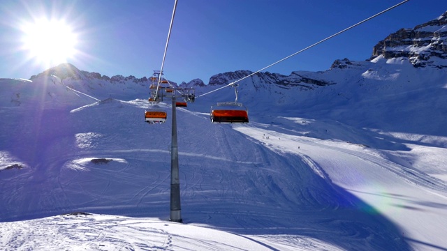 在德国Zugspitze滑雪场，POV坐在橙色泡泡滑雪椅上，在日落前有柱子和地平线上的太阳反射的斜坡上视频下载