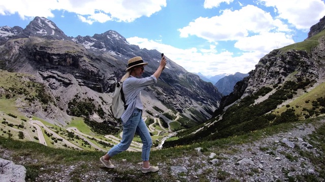 白人女游客享受令人惊叹的自然行走在山的山丘，微笑的潮女旅游与背包拍照手机相机视频素材