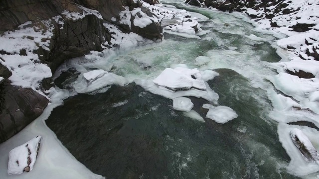 在俄罗斯高加索山脉的一个被白雪覆盖的峡谷底部，一条湍急的山间溪流的碧绿的水视频素材