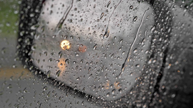 雨点打在汽车的侧窗上。从后视镜反射出来的过往汽车的模糊灯光。水珠从玻璃表面滑落。从车里看，超高清视频素材