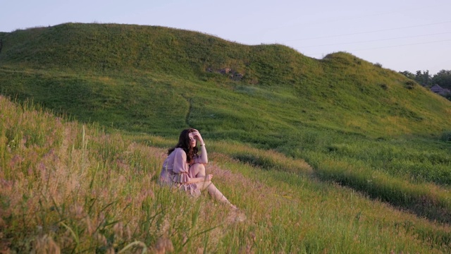 美丽的女孩坐在一片充满阳光的草地上，穿着浪漫的衣服，年轻女子享受自然，概念女性美视频素材