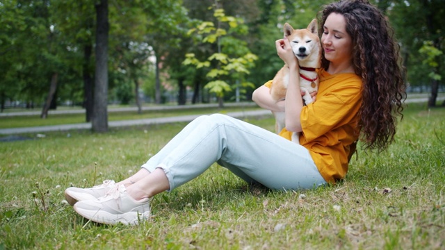 漂亮的年轻女子亲吻狗嘴和微笑坐在草地上的公园视频素材