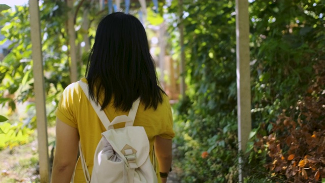 慢镜头亚洲女人走在花园里的树巷在阳光明媚的一天视频素材