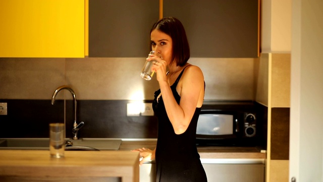 年轻美丽的女人在她的现代厨房里喝水。清晨的水合作用视频素材