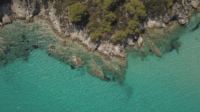 鸟瞰图的小海滩与绿松石水旁边的岩石和树木在Agia Paraskevi Halkidiki地区，希腊。从无人机视频素材