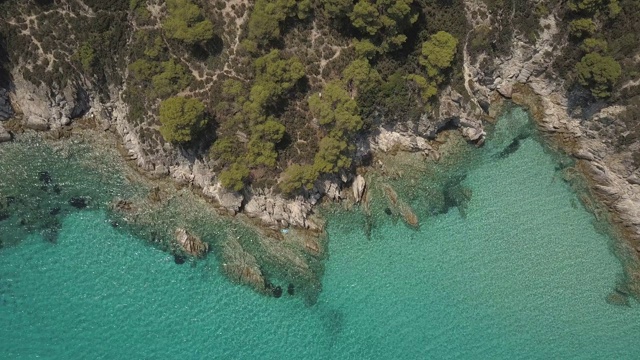 鸟瞰图的小海滩与绿松石水旁边的岩石和树木在Agia Paraskevi Halkidiki地区，希腊。从无人机视频素材