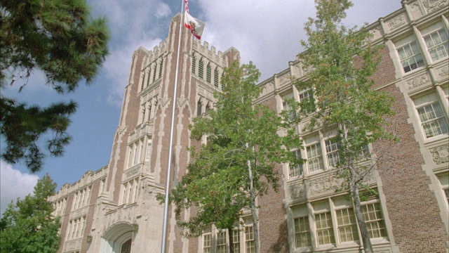 三层砖砌建筑，可以是高中或学院，大学，常青藤联盟校园，美国国旗和加州国旗旗杆在fg。视频素材