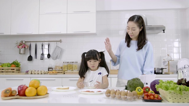 快乐的亚洲家庭妈妈看小女孩正在吃早餐，麦片和牛奶在家里的厨房。健康食品理念为了增强身体的力量视频素材