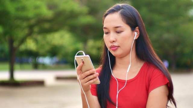 女人用手机听音乐，在公园里放松视频素材