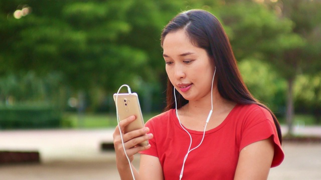 女人用手机听音乐，在公园里放松视频素材