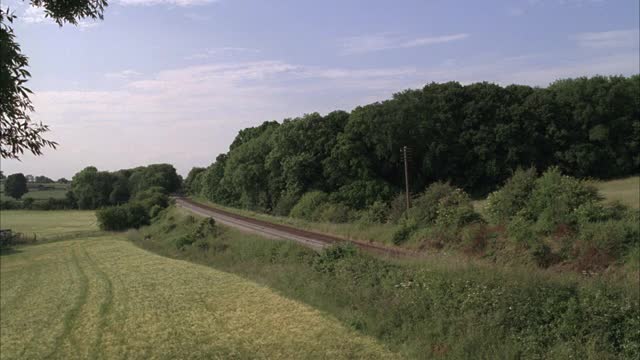 旅客列车在铁路轨道上行驶，通过农村或农村地区。树木和草，草地或田野。可能是格洛斯特郡的斯特劳德。20 FPS。视频素材