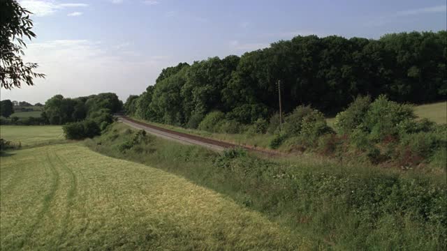 旅客列车在铁路轨道上行驶，通过农村或农村地区。树木和草，草地或田野。可能是格洛斯特郡的斯特劳德。20 FPS。视频素材