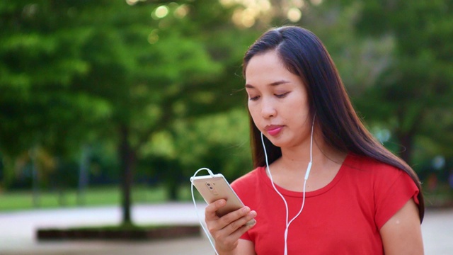 女人用手机听音乐，在公园里放松视频素材