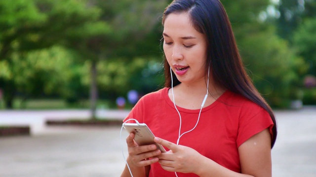 女人用手机听音乐，在公园里放松视频素材