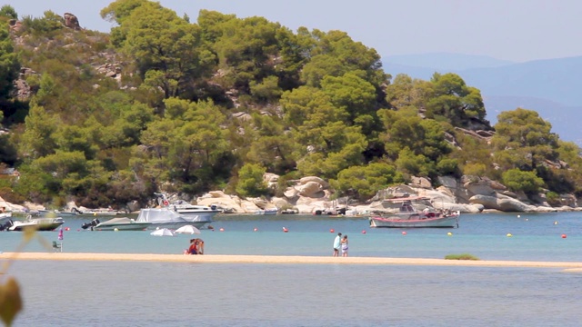 希腊Halkidiki，有游艇和渔船的田园诗般的海滩，海边有树木的岩石视频素材