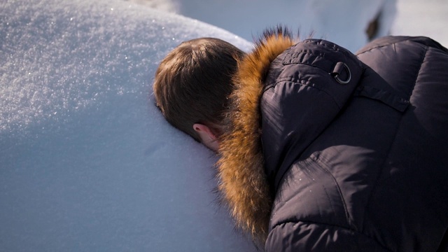 一个穿着冬季夹克的男人在雪堆上留下了他的脸视频素材